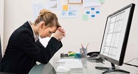Woman at desk looking concerned in front of a computer screen with a spreadsheet
