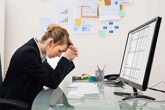 Woman at desk looking concerned in front of a computer screen with a spreadsheet