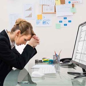 Woman at desk looking concerned in front of a computer screen with a spreadsheet